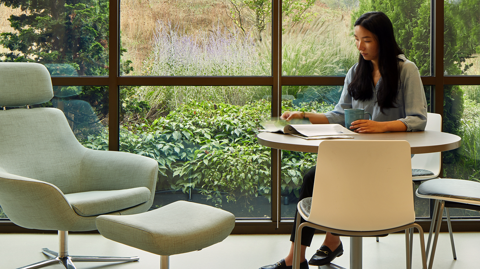 A staff member sits in the staff break room reading a magazine in front of large windows with views to nature