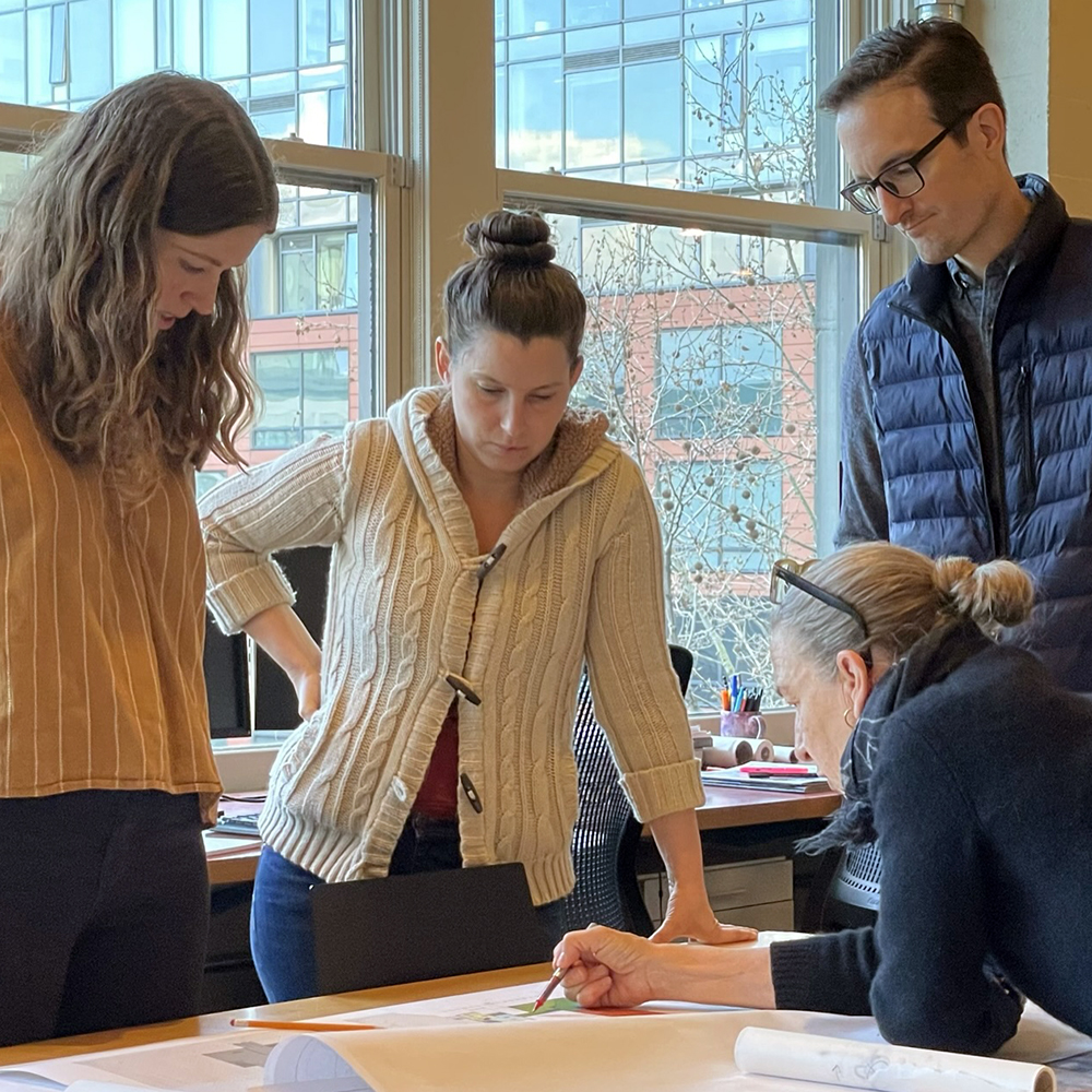 Four people stand around a table while one person sketches an idea.